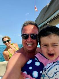 A joyful family captures a fun moment on a boat, showcasing smiles and excitement in a beautiful marine setting.