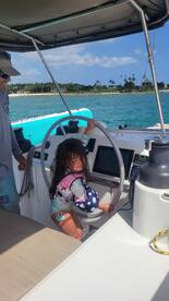 A young girl playfully engages with the helm of a boat while an adult supervises, showcasing the fun of boating experiences for families.