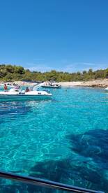 A vibrant scene of boats anchored in crystal-clear waters, with people enjoying the beach and swimming — a perfect summer getaway.