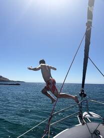 A person leaps off the bow of a boat into the sparkling blue waters, capturing the essence of summer fun and adventure on the water.