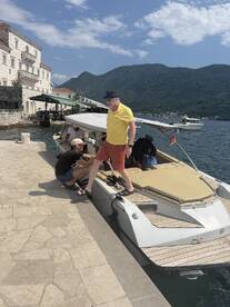 A lively scene at the dock with a group preparing to board a boat, set against a stunning mountainous backdrop — perfect for summer adventures on the water.