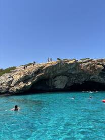 A vibrant scene of people swimming in crystal-clear waters near a stunning rock formation, showcasing the beauty of a perfect summer day on the water.