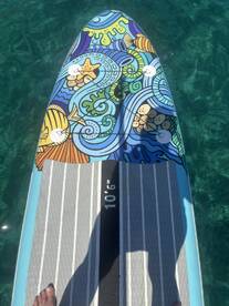 A vibrant paddleboard with artistic designs floats on clear waters, perfect for enjoying a day of fun on the water.