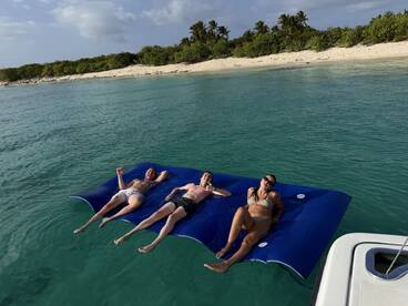 A group of friends relaxes on a floating mat in crystal-clear waters, enjoying a perfect day at the beach — ideal for sunbathing and fun in the sun.