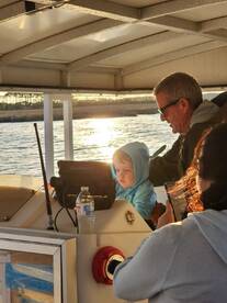 A heartwarming moment on a boat as a child and adult engage at the helm during sunset, capturing the joy of family time on the water.