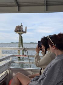 Two friends capture a moment on a boat, enjoying the scenic view of a bird's nest on a post — a perfect blend of nature and adventure.