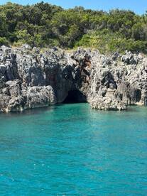 A stunning view of a rocky coastline featuring a cave entrance, surrounded by crystal-clear turquoise waters — a perfect destination for exploration and adventure.