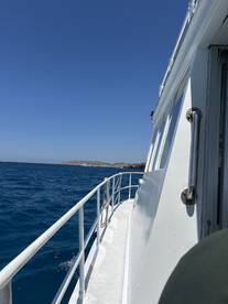 A clear view of the side of a boat cruising through vibrant blue waters, showcasing the vessel's structure against a sunny sky.