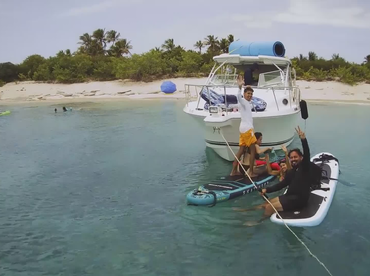 A lively group enjoys a fun day on the water, paddleboarding and swimming near a boat, creating unforgettable beach memories.