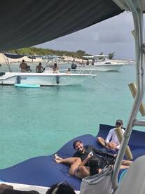 A fun group enjoys a day on the water, relaxing on a floating mat while surrounded by boats and beautiful scenery — perfect for a lively beach outing.