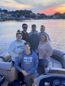 A cheerful group poses for a photo on a pontoon boat at sunset, capturing a memorable moment on the water — perfect for family gatherings or celebrations.
