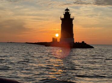 A stunning sunset behind a lighthouse, casting a warm glow over the water — a picturesque moment perfect for capturing the beauty of coastal landscapes.