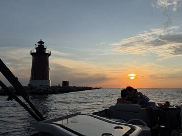 A group enjoys a picturesque sunset view near a lighthouse, creating a perfect backdrop for memorable moments on the water.
