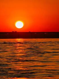A breathtaking sunset casts vibrant orange hues over the water, creating a serene backdrop perfect for evening boat cruises.