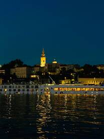 A beautifully illuminated boat glides along the river at night, reflecting the vibrant cityscape and creating a picturesque scene perfect for evening cruises.