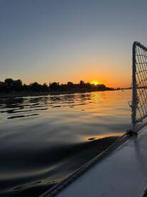 A serene sunset view from the side of a boat, showcasing tranquil waters and a picturesque shoreline — perfect for evening cruises.