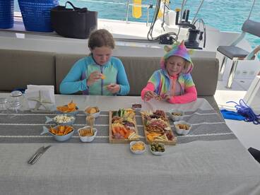 Two children enjoy a colorful spread of snacks and charcuterie aboard a boat, perfect for family outings and fun on the water.