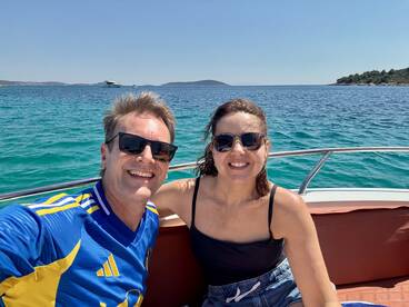 A cheerful couple enjoys a sunny day on the boat, capturing the perfect moment with stunning turquoise waters in the background.