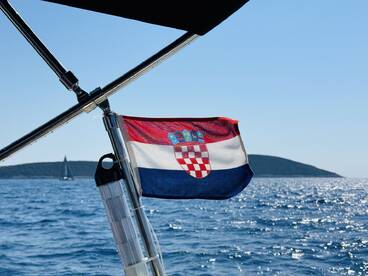 A vibrant Croatian flag flutters on a sailboat, with a picturesque island in the background, capturing the essence of sailing in the beautiful Adriatic Sea.