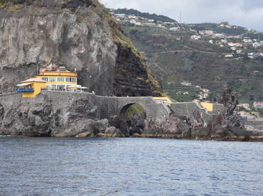 A scenic view of a coastal area featuring a vibrant yellow building and people enjoying the rocky shoreline — a perfect destination for beachgoers and nature lovers.