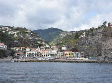 A picturesque view of a coastal town nestled among lush hills, showcasing charming architecture and a serene harbor — perfect for exploring the beauty of Madeira.