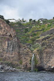 A stunning view of a waterfall cascading down rocky cliffs, surrounded by lush greenery and terraced landscapes, showcasing the natural beauty of the coastline.