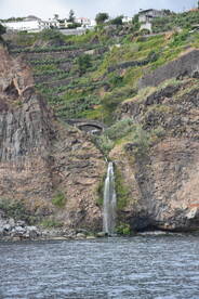 A stunning waterfall cascades down rocky cliffs, surrounded by lush greenery, showcasing the natural beauty of the coastline.