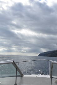A serene view from the bow of a boat, showcasing the expansive ocean and distant coastline under a cloudy sky — perfect for exploring coastal waters.
