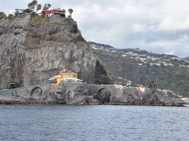 A picturesque view of a coastal landmark with a vibrant yellow building perched on the rocky cliffs, showcasing the stunning landscape of Madeira.