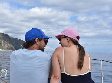 A couple enjoys a romantic moment on a boat, gazing at the ocean and mountains in the background — perfect for memorable getaways.