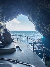 Guests enjoy a scenic view from a boat as it navigates through a cave, showcasing the stunning ocean beyond — a perfect adventure for exploration lovers.