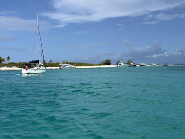 A picturesque view of a sailboat navigating through clear turquoise waters, surrounded by other vessels and a sandy shoreline, perfect for showcasing boating adventures.