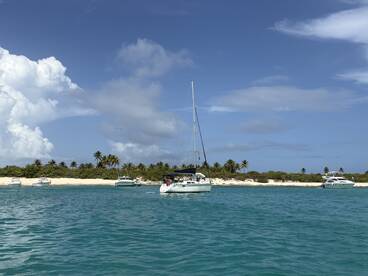 A serene view of a sailboat anchored in turquoise waters, surrounded by lush greenery and sandy beaches — a perfect setting for a relaxing day on the water.
