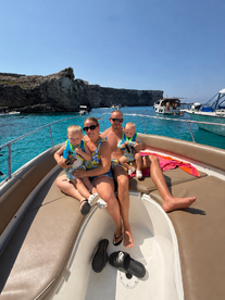 A joyful family enjoys a sunny day on a boat, surrounded by stunning turquoise waters and rocky cliffs — perfect for summer adventures and family bonding.