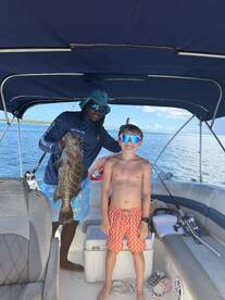 A young boy proudly poses with a large fish alongside his captain on a boat, capturing a memorable fishing experience on the water.