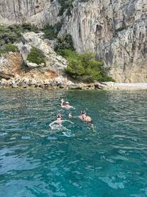 A group enjoys snorkeling in crystal-clear waters, surrounded by stunning rocky cliffs — a perfect adventure for water enthusiasts.