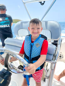 A young boy joyfully steers a boat while wearing a life jacket, capturing the excitement of family boating adventures.