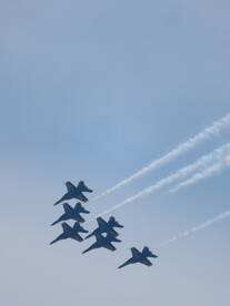 A formation of jets performing aerial maneuvers against a clear sky, showcasing precision flying.