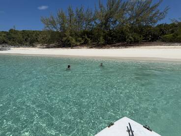 Two individuals enjoy a refreshing swim in the crystal-clear waters of a secluded beach, surrounded by lush greenery — a perfect tropical getaway.