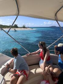 A group of friends enjoys a scenic view from their boat, looking towards a beautiful island and beach — perfect for a day of adventure on the water.