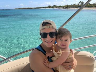 A joyful moment captured on a boat, featuring a smiling father holding his baby against a stunning ocean backdrop — perfect for family outings on the water.