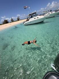 A woman enjoys a refreshing swim in crystal-clear waters near a boat, capturing the essence of a perfect beach day filled with fun and relaxation.