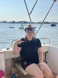 A young girl poses playfully in a captain's hat on a boat, capturing a fun moment during a day on the water — perfect for family outings and celebrations.