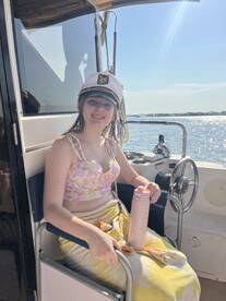 A young girl sits comfortably in the helm area of a boat, wearing a captain's hat and enjoying a sunny day on the water. Perfect for family outings and boating adventures.