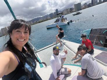 A joyful group enjoys a sunny day on a catamaran, capturing memories with smiles and laughter against a stunning ocean backdrop.