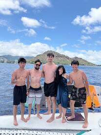 A joyful group of friends poses together on a boat, enjoying a sunny day on the water with stunning mountain views in the background — perfect for memorable beach outings.