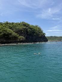 A couple enjoys a refreshing swim in the clear turquoise waters near a lush coastline, perfect for a relaxing day on the water.