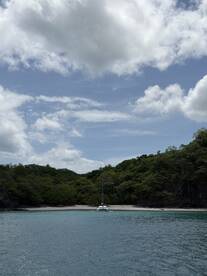 A serene view of a catamaran anchored in a secluded bay, surrounded by lush greenery and clear waters — an ideal spot for relaxation and exploration.
