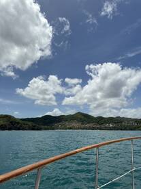 A scenic view from the bow of a boat, showcasing lush green hills and a vibrant sky, perfect for capturing the essence of a tranquil day on the water.