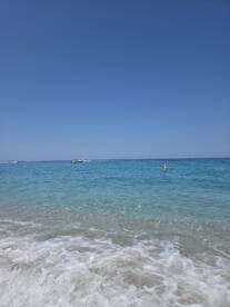 A serene view of a clear turquoise coastline with gentle waves lapping at the shore, perfect for a relaxing beach day.
